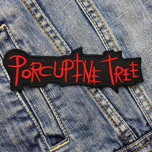 Può includere: Toppa rettangolare nera con le parole "Porcupine Tree" ricamate in rosso. La toppa è su una giacca di jeans blu. Il testo è in un font stilizzato.