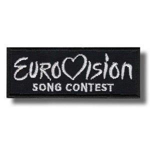 Könnte beinhalten: Ein rechteckiger schwarzer Aufnäher mit weiß gesticktem Text. Der Text lautet "Eurovision" mit einem Herzsymbol anstelle des "o" und "Song Contest" darunter. Der Aufnäher hat eine strukturierte Oberfläche.