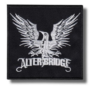 Op de afbeelding: Zwart vierkantige patch met een wit geborduurd adelaarsontwerp en de bandnaam "ALTER BRIDGE" in een gestileerd lettertype. De adelaar heeft uitgespreide vleugels en de patch heeft een zwarte rand.