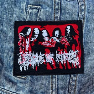 May include: Black rectangular patch with a red and white design. The patch features a stylized illustration of figures and the band name "Cradle of Filth" in white, gothic-style lettering.
