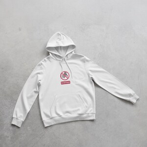 Peut inclure: Sweat &agrave; capuche blanc avec une poche avant et une capuche &agrave; cordon. Le sweat-shirt pr&eacute;sente un graphisme rouge et blanc d'une main avec un symbole de cercle et de barre rouge, et les mots "Do not touch" en dessous.