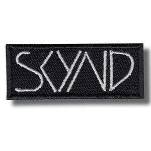 Könnte beinhalten: Ein rechteckiger schwarzer Aufnäher mit dem Wort "SYND" in Weiß gestickt. Die Buchstaben sind in einer modernen Schriftart gestaltet. Der Aufnäher hat einen schwarzen Rand und ist wahrscheinlich zum Aufnähen auf Kleidung oder Accessoires bestimmt.