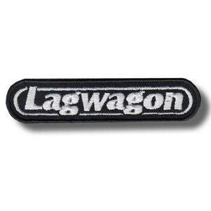 May include: A black and white embroidered patch with the word "Lagwagon" in white, stylized text. The patch is rectangular with rounded corners and a black border. The patch is likely for clothing or accessories.
