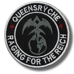 May include: A round, black patch with white embroidered text and a gray emblem. The text reads "QUEENSRYCHE" and "RACING FOR THE REICH". The emblem is a stylized design with a central figure and wings. Two red crosses are on either side.