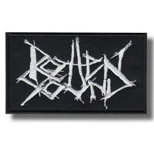 Puede incluir: Parche rectangular negro con texto blanco bordado. El texto está estilizado y parece ser un logotipo de banda. El parche tiene un borde negro y probablemente está hecho de tela.