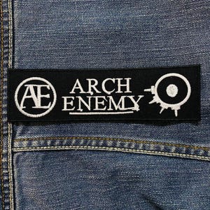 May include: A black rectangular patch with the words "ARCH ENEMY" in white, along with a circular logo and the letters "AE". The patch is sewn onto a blue denim fabric, showcasing a classic rock and roll aesthetic.