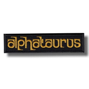 May include: Black rectangular patch with the word "alphataurus" embroidered in gold thread. The patch has a black border and a slight shadow effect, giving it a three-dimensional appearance. The text is in a stylized font.