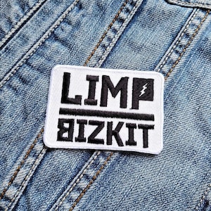 Könnte beinhalten: Ein weißes rechteckiges Patch mit schwarzem gesticktem Text, der "LIMP BIZKIT" mit einem Blitz-Grafik liest. Der Patch ist auf eine blaue Jeansjacke genäht.