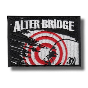 Op de afbeelding: Een rechthoekige zwarte patch met de witte tekst "ALTER BRIDGE". De patch heeft een rood-wit doelontwerp met een zwart silhouet. Deze patch is waarschijnlijk voor een band of muziekgroep.