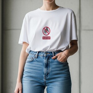 Peut inclure: T-shirt blanc avec un motif rouge et noir d'une main barr&eacute;e d'un cercle et les mots "Do not touch" en dessous. Le t-shirt est port&eacute; avec un jean bleu.