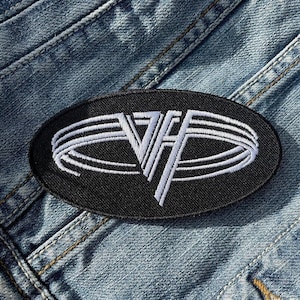 Op de afbeelding: Zwarte ovale patch met de witte gestileerde letters "VH" in een wit ovaal ontwerp. De patch bevindt zich op een blauw spijkerjasje.