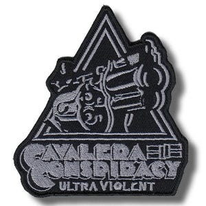 Può includere: Toppa ricamata nera e grigia con la scritta "CAVALERA CONSPIRACY" e "ULTRA VIOLENT". La toppa presenta un design triangolare con un'illustrazione stilizzata di una figura su una moto. Adatta per essere cucita su abiti o borse.