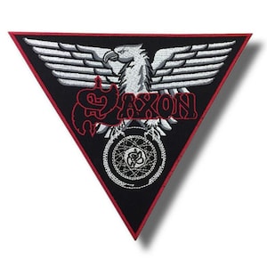 Może przedstawiać: Trójkątna czarna naszywka z czerwoną obwódką przedstawia białego orła z rozpostartymi skrzydłami. Słowo "SAXON" jest wyhaftowane na czerwono, a na dole znajduje się okrągły wzór.