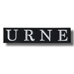 May include: Black rectangular patch with the word "URNE" embroidered in white capital letters. The patch has a black border and a shadow effect, creating a three-dimensional appearance. The letters are in a serif font.