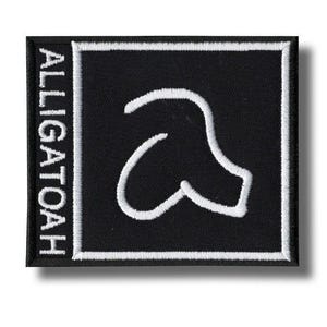 May include: A square black patch with a white border and the word "ALLIGATOAH" vertically on the left. The patch features a white, stylized "a" shape in the centre.