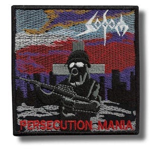 Könnte beinhalten: Gestickter Aufnäher mit einem Soldaten mit Gasmaske und Gewehr, vor dem Hintergrund eines Kreuzes und einer Stadtlandschaft. Der Aufnäher trägt den Bandnamen "Sodom" in Weiß und den Text "PERSECUTION MANIA" in Rot.