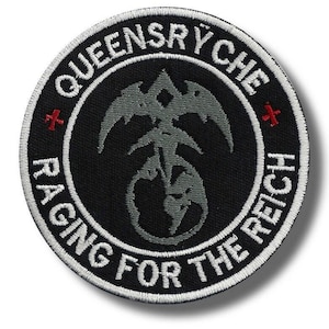 May include: A round, black embroidered patch with white text and a gray emblem. The text reads "QUEENSRYCHE" and "RACING FOR THE REICH". The emblem is a stylized design with a bird-like shape. Two red crosses are on the patch.