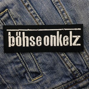 May include: A black rectangular patch with the white text "böhse onkelz" embroidered on it. The patch is set against a denim jacket background. The text is in a bold, stylized font.