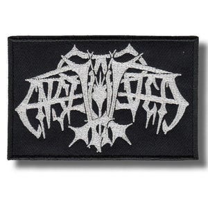 May include: Black rectangular patch with white stylized text. The text appears to be a band logo or emblem, featuring sharp, angular lines and a gothic aesthetic. The patch is likely made of fabric and designed to be sewn or ironed onto clothing or accessories.