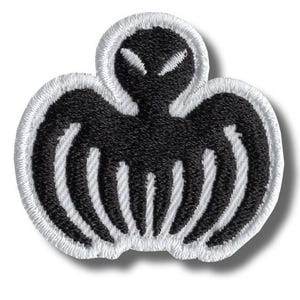 May include: Embroidered patch with a black alien-like design, white accents, and a white border. The symmetrical shape features a head and wing-like elements. Suitable for application on clothing or accessories.
