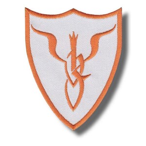 May include: Shield-shaped embroidered patch with a white background and an orange border. The patch features an orange stylized design in the centre. Suitable for application on clothing or accessories.