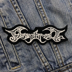 Puede incluir: Parche bordado en blanco y negro con la palabra "Symphony of Destruction" en una fuente estilizada. El parche es rectangular con bordes curvos y está cosido a una chaqueta vaquera.