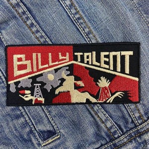 Peut inclure: Écusson rectangulaire avec le texte "BILLY TALENT" en blanc, rouge et noir. L'écusson présente un design stylisé avec un fond rouge et noir, cousu sur une veste en jean.