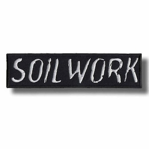 May include: A black rectangular patch with the white embroidered text "SOIL WORK". The patch has a black border and is likely designed to be sewn or ironed onto clothing or accessories. The text is in a stylized, handwritten font.