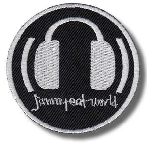 Puede incluir: Parche redondo negro con un diseño bordado en blanco de auriculares. El texto "Jimmy Eat World" está bordado en blanco debajo de los auriculares, dentro del círculo.