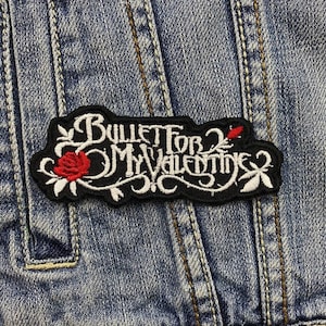Könnte beinhalten: Ein schwarzer, gestickter Aufnäher mit dem Text "Bullet for My Valentine" in weißer Schrift. Der Aufnäher zeigt eine rote Rose und dekorative florale Elemente. Der Aufnäher ist auf eine blaue Jeansjacke genäht.