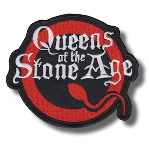 Pode incluir: Patch bordado com o texto "Queens of the Stone Age" em branco, com letras góticas. O texto está sobre um fundo preto dentro de um design circular vermelho. O patch tem uma borda preta.