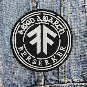 May include: Round black and white embroidered patch with the words "BLOOD AMARCH BERSERKER" around the edge. The center features a white symbol. The patch is sewn onto a denim jacket.