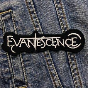 May include: Black and white embroidered patch featuring the band name "Evanescence". The patch has a unique shape with the band's name in a stylized font. The patch is set against a denim background.