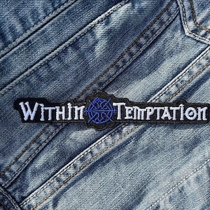 Puede incluir: Parche bordado en blanco y negro con el texto "Within Temptation". Presenta un emblema azul en el centro, sobre un fondo de mezclilla azul.