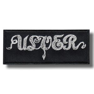 Könnte beinhalten: Schwarzer rechteckiger Aufnäher mit dem Wort "USTER" in weiß gestickter, stilisierter Schrift. Der Aufnäher hat einen schwarzen Rand und ein weißes Stickdesign. Das Design ist eine dekorative Schreibschrift.