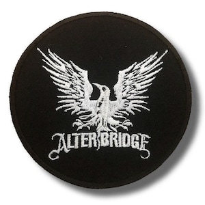 Op de afbeelding: Een ronde, zwarte patch met een wit geborduurd ontwerp van een vogel met uitgespreide vleugels. De tekst "ALTER BRIDGE" is eronder in het wit geborduurd. De patch heeft een zwarte rand.