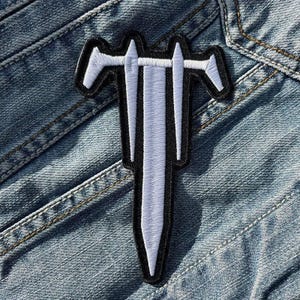 Peut inclure: Écusson de sabre blanc avec bordure noire, brodé sur une veste en jean. L'écusson présente un motif d'épée stylisée avec une longue lame et deux barres transversales. L'écusson est rectangulaire et a une esthétique épurée et moderne.