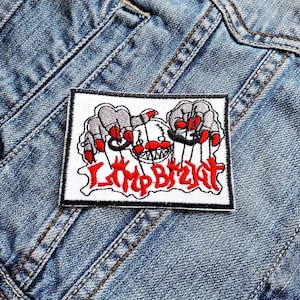 May include: A rectangular white patch with the text "Limp Bizkit" in red, stylized lettering. The patch features a cartoon design of gray hands with red fingertips and a white face with a red nose and mouth.