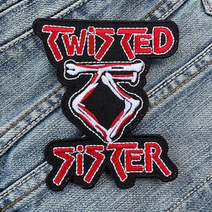 Puede incluir: Parche bordado en negro y rojo con las palabras "TWISTED SISTER". El parche presenta un diseño en forma de diamante blanco y rojo en el centro. El parche está cosido en una chaqueta vaquera.