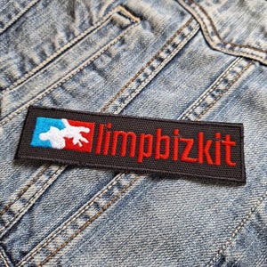 Op de afbeelding: Een rechthoekige zwarte patch met de rode tekst "limpbizkit" en een afbeelding in wit, blauw en rood. De patch is op een spijkerjas genaaid.