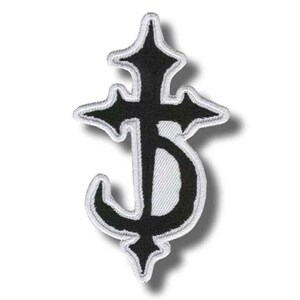 Puede incluir: Parche bordado en blanco y negro con un diseño de cruz estilizada. El parche tiene una forma de cruz negra con un borde blanco y una parte inferior curva. El parche es probablemente para ropa o accesorios.