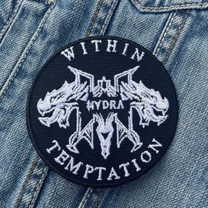 Op de afbeelding: Een ronde, zwarte patch met witte geborduurde tekst en een grafisch ontwerp. De tekst luidt "WITHIN HYDRA TEMPTATION". De patch bevindt zich op een spijkerjasje.