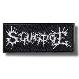 Puede incluir: Parche rectangular negro con la palabra "SLUDGE" bordada en blanco en una fuente gótica puntiaguda. El parche es probablemente para ropa o accesorios y tiene una textura tejida.
