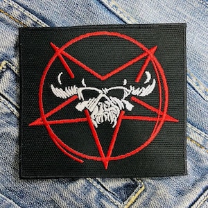 Może przedstawiać: Czarna kwadratowa naszywka z czerwonym pentagramem otaczającym białą czaszkę z rogami. Naszywka jest haftowana szczegółowym wzorem. Naszywka jest prawdopodobnie przeznaczona na odzież lub akcesoria.