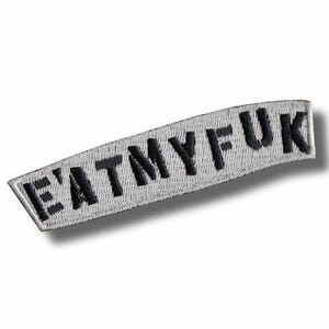 Op de afbeelding: Een rechthoekige, gebogen patch met de geborduurde tekst "EATMYFUK" in zwarte hoofdletters. De patch heeft een witte achtergrond en een zwarte rand. De patch is ontworpen om op kleding of accessoires te worden genaaid.