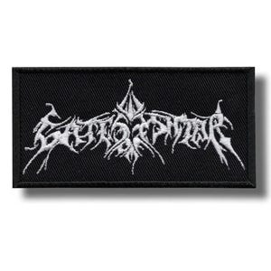 May include: Black rectangular patch with white embroidered text. The text is stylized and appears to be a band logo or emblem. The patch has a black border and is likely made of fabric.