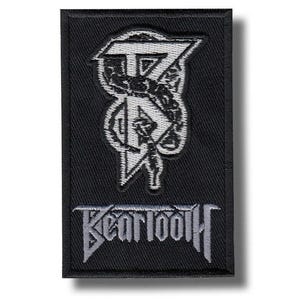 May include: Black rectangular patch with a white and grey emblem and the word "BEARTOOTH". The emblem has a unique design with geometric shapes and a figure, in a stylized font.