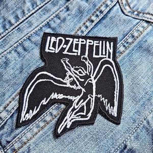 Op de afbeelding: Zwart en wit geborduurde patch met het Led Zeppelin-logo en het iconische Icarus-beeld. De patch is rechthoekig met een unieke vorm en is genaaid op een spijkerjasje. Een accessoire met een muzikaal thema.