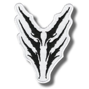 Può includere: Toppa ricamata con un design nero astratto su sfondo bianco. Il design è simmetrico, con bordi appuntiti e linee curve, che assomiglia a un volto di animale stilizzato o a un simbolo tribale. La toppa ha un bordo bianco.