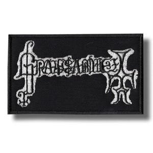 Può includere: Toppa rettangolare nera con testo ricamato bianco ed elementi decorativi. Il testo sembra essere il nome o il logo di una band. La toppa è probabilmente per abbigliamento o accessori.